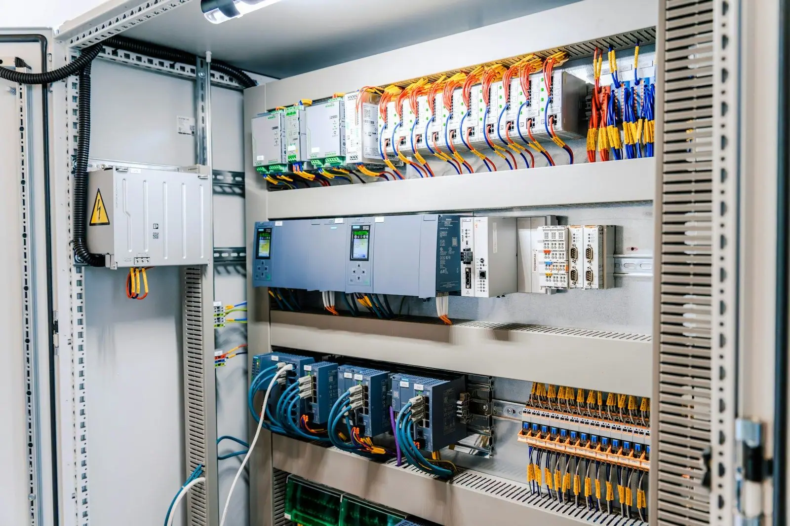 The inside of an open industrial control cabinet with drives, controllers and terminal blocks